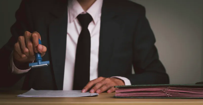 Funcionario con traje sellando un documento oficial sobre un escritorio