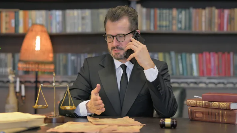 Abogado hablando por teléfono en su despacho junto a una balanza de la justicia y libros de derecho