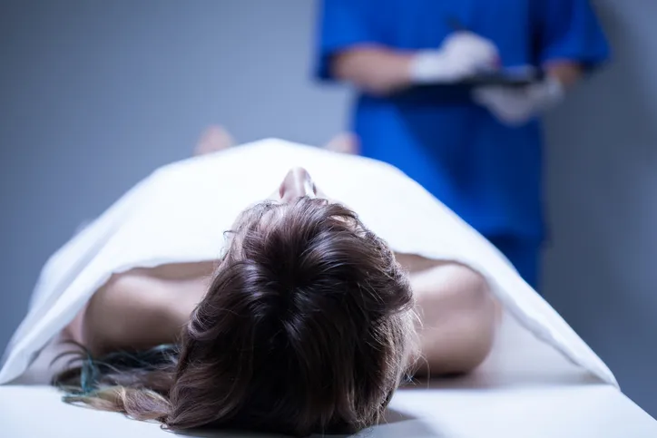 Profesional sanitario examinando un cadáver cubierto con una sábana en la morgue