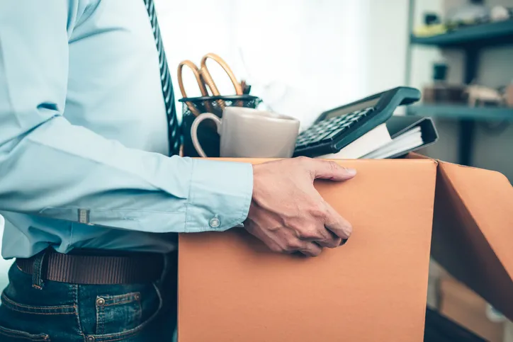 Hombre cargando una caja con objetos de oficina como una taza, una calculadora y bolígrafos, tras dejar su puesto de trabajo.