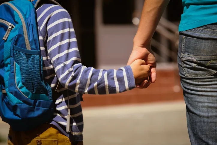 Niño con mochila escolar cogido de la mano de un adulto, imagen relacionada con la custodia y cuidado de los hijos