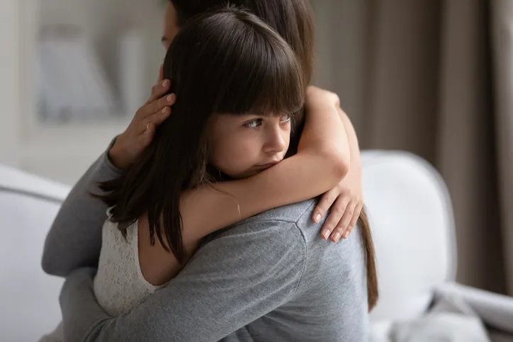 Madre abrazando a su hija pequeña, que mira preocupada, transmitiendo apoyo emocional en un momento familiar difícil