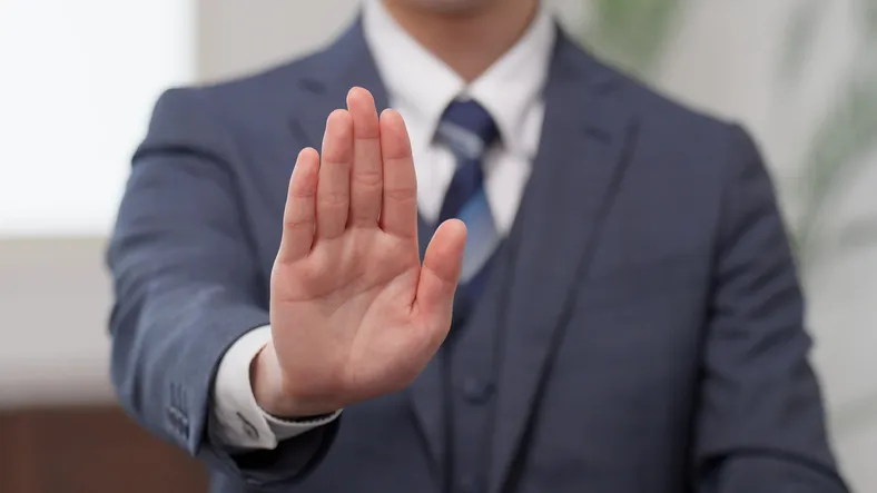 Hombre de traje haciendo el gesto de 'stop' con la mano extendida hacia la cámara.