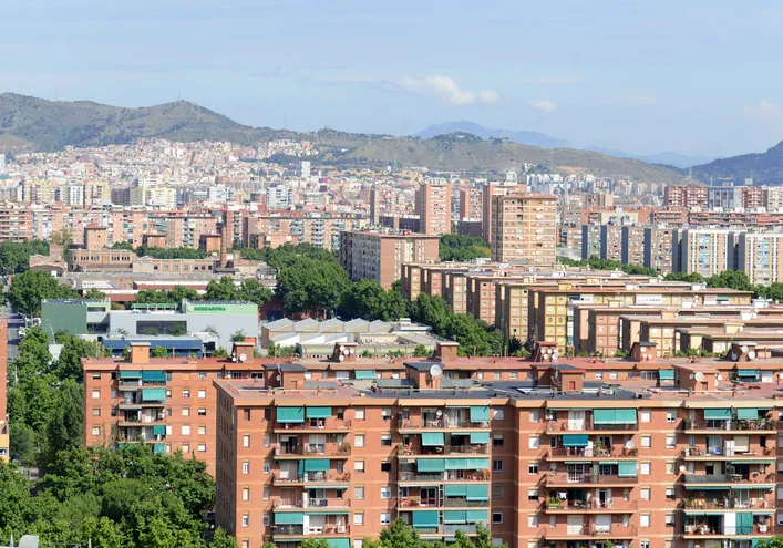 Vista panorámica de una ciudad con numerosos edificios residenciales rodeados de vegetación y montañas al fondo.