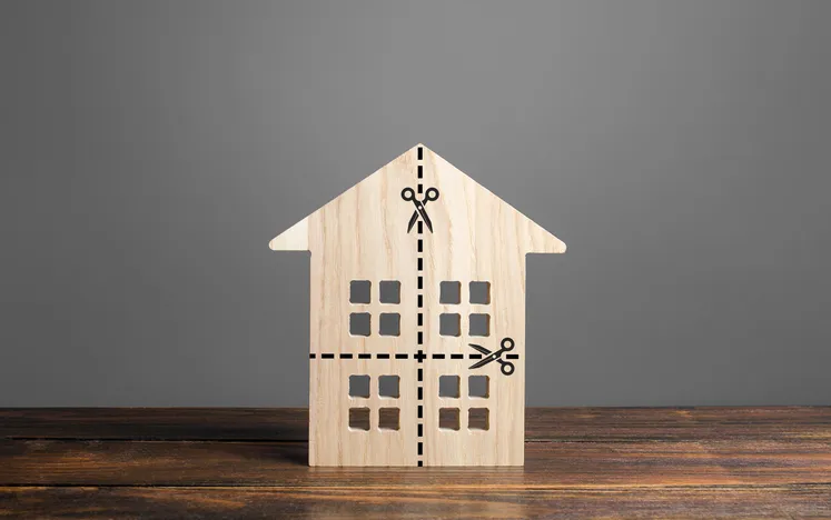 Casa de madera con líneas de corte marcadas en cuatro partes, simbolizando el reparto de una vivienda heredada entre varios herederos