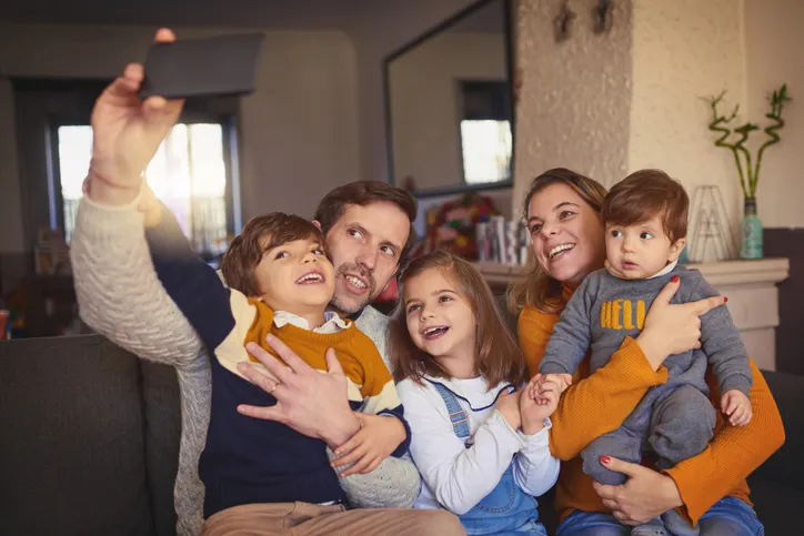 Familia sonriente con tres niños haciéndose una fotografía juntos en el salón de su casa.