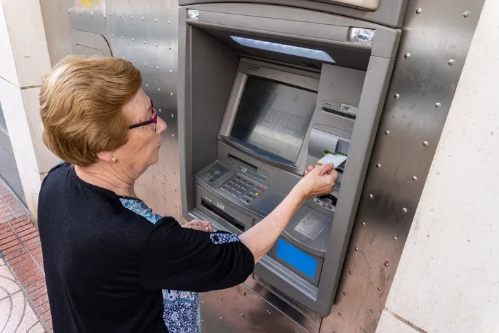 Mujer mayor retirando dinero en efectivo con su tarjeta en un cajero automático en la calle