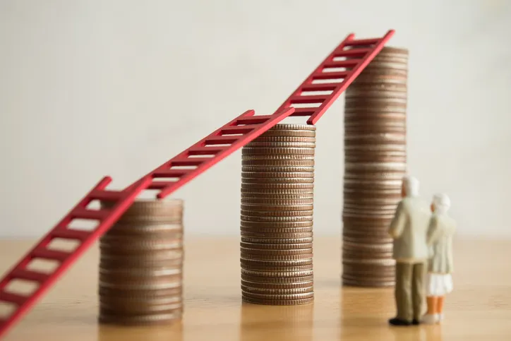 Figuras de jubilados junto a escalera roja sobre pilas de monedas, simbolizando el crecimiento de la pensión