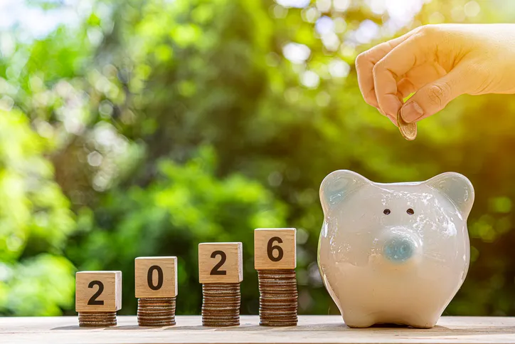 Hucha de ahorro con monedas apiladas junto a bloques de madera que forman el número 2026, simbolizando el ahorro para la jubilación"