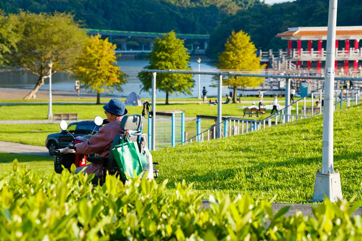 Persona mayor circulando en scooter de movilidad por un parque junto a un lago