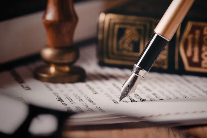 Pluma estilográfica firmando un documento legal junto a un sello notarial, representando la redacción de un testamento