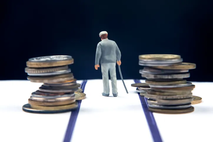 Figura de un anciano con bastón caminando entre dos caminos flanqueados por pilas de monedas