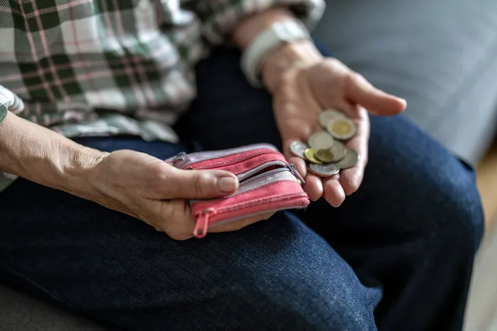 Persona mayor contando monedas sueltas en la mano junto a un monedero rosa