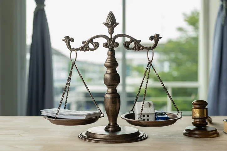 Balanza de la justicia con documentos y una casa en miniatura, junto a un mazo de juez sobre una mesa