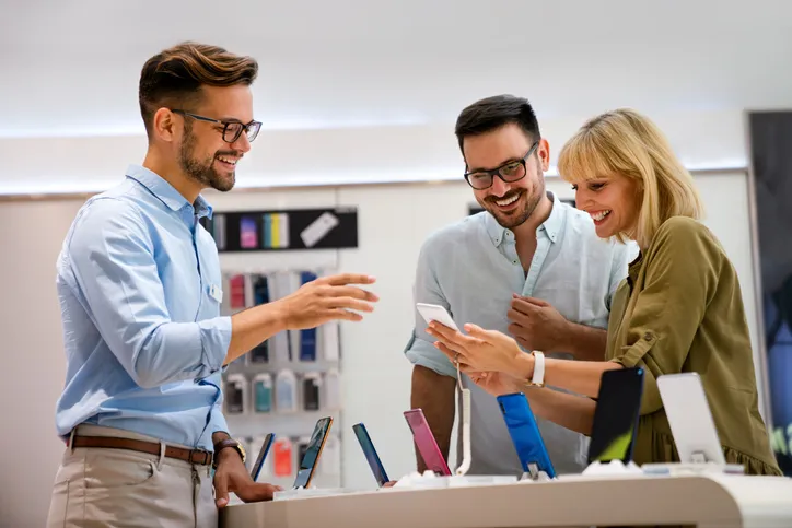 Vendedor mostrando un móvil a una pareja de clientes en una tienda de tecnología