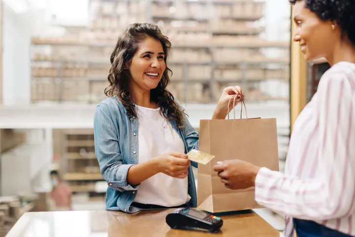 Clienta pagando con tarjeta al recoger una bolsa de compra en una tienda