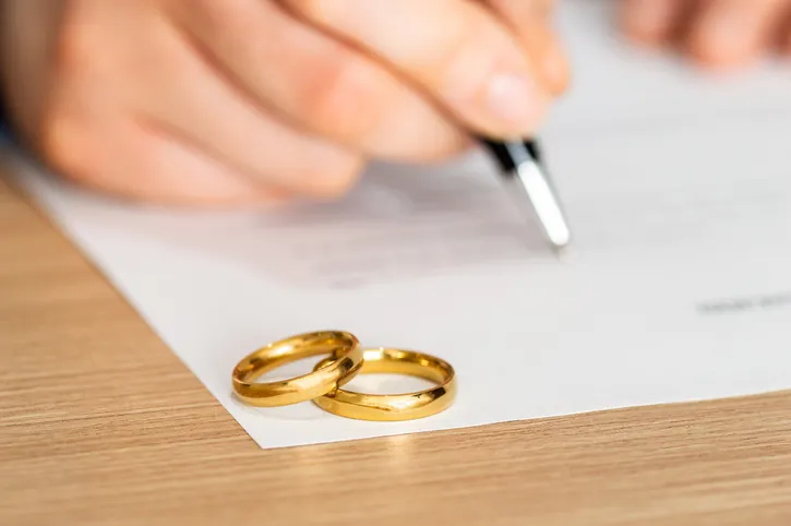 Dos alianzas de boda sobre un documento que una persona está firmando, representando la formalización de un matrimonio