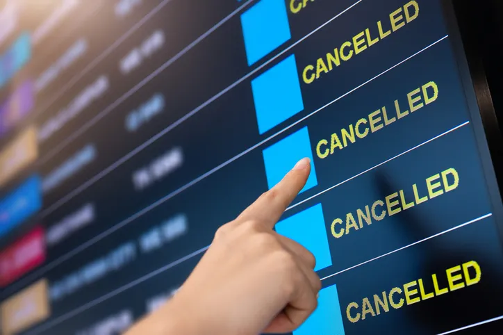 Dedo señalando una pantalla de aeropuerto con varios vuelos marcados como cancelados
