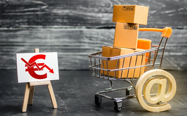 Carrito de la compra con cajas, un símbolo de arroba y un cartel de euro a la baja