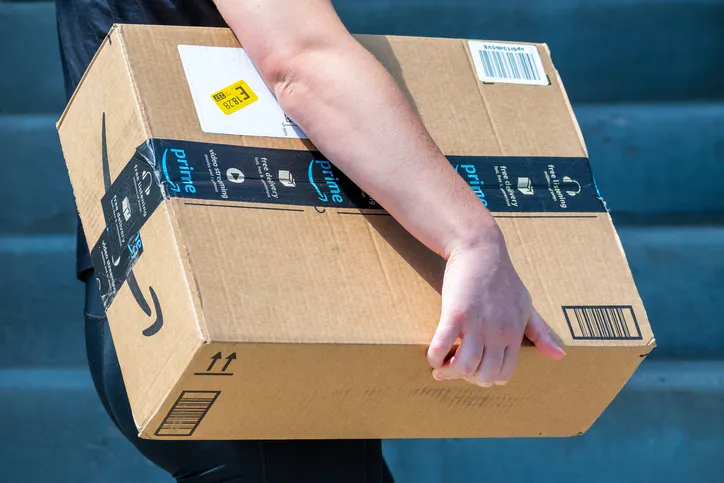 Repartidor sujetando una caja de cartón con cinta de Amazon Prime en unas escaleras