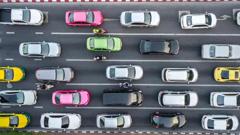 Vista aérea de una avenida con varios carriles llenos de coches de colores y motos circulando en tráfico denso