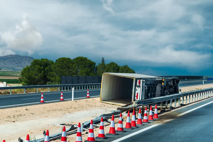 Camión volcado en el arcén de una autopista tras un accidente de tráfico, señalizado con conos