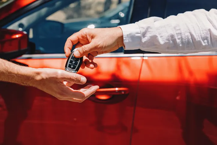Entrega de las llaves de un coche rojo entre dos personas tras una compraventa