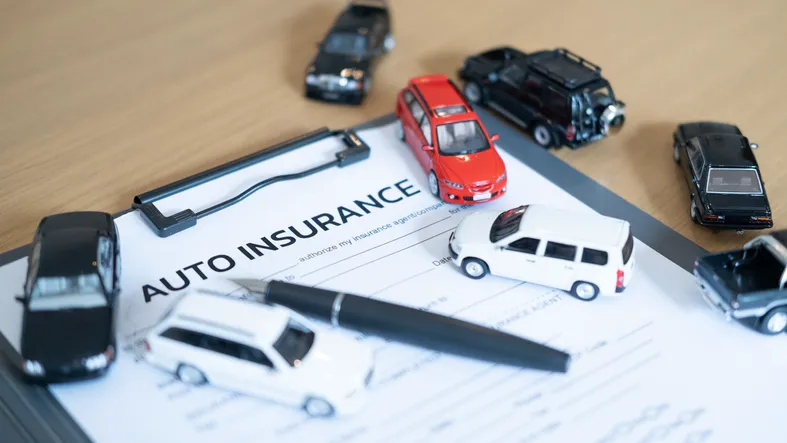 Formulario de seguro de coche rodeado de vehículos en miniatura y un bolígrafo