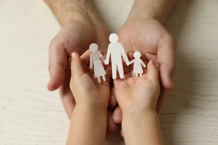 Manos de un adulto y un niño sosteniendo juntas una figura de papel de una familia, simbolizando la unión familiar en la adopción