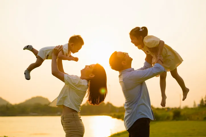 Padres levantando en brazos a sus dos hijos al atardecer junto a un lago
