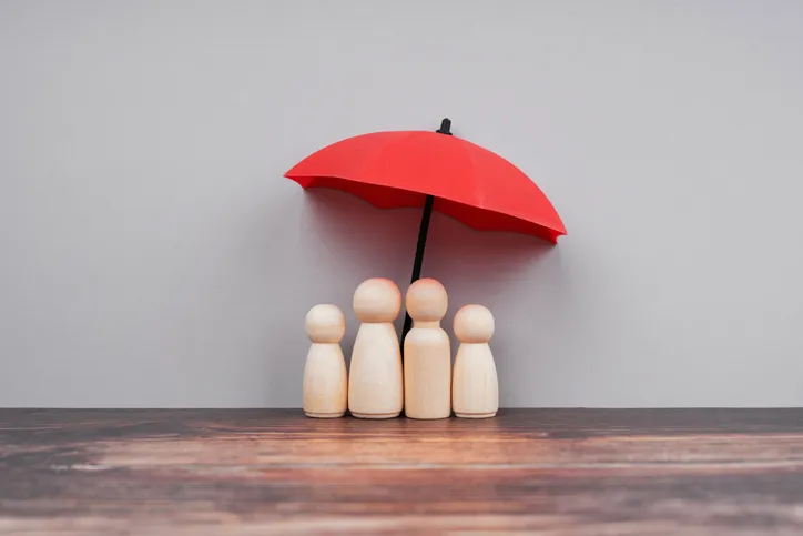Cuatro figuras de madera representando a una familia bajo un paraguas rojo en miniatura