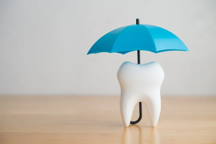 Figura de una muela protegida por un pequeño paraguas azul, simbolizando el seguro dental