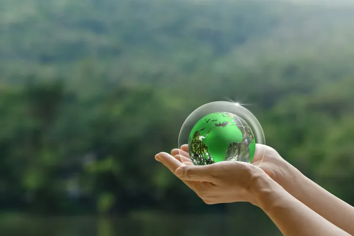 Manos sosteniendo un pequeño globo terráqueo verde rodeado de una burbuja protectora
