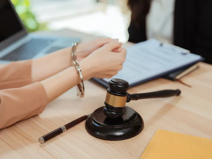Persona esposada sentada ante una mesa con un mazo de juez y documentos legales