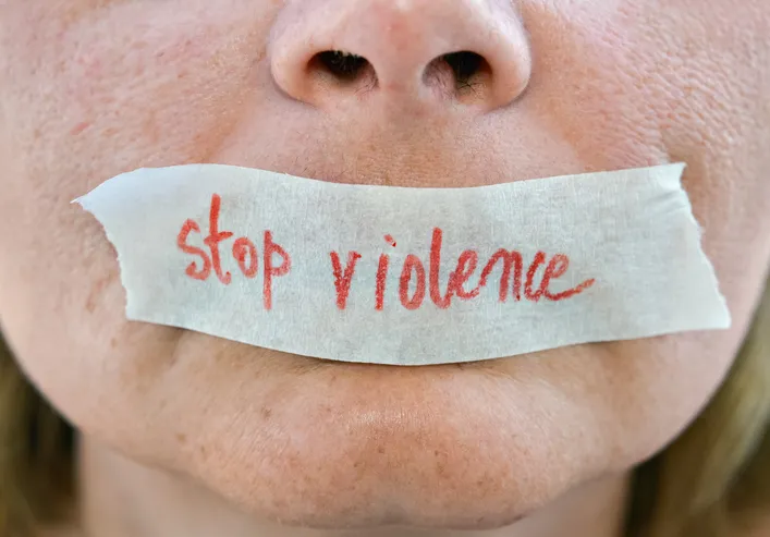 Primer plano de una boca tapada con cinta donde está escrito 'stop violence', simbolizando el silencio impuesto a las víctimas de violencia de género
