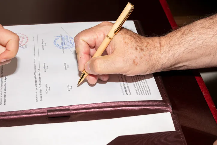 Firma de un documento oficial de matrimonio con bolígrafo sobre carpeta de cuero