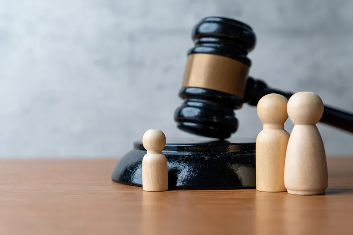 Figuras de madera representando una familia junto a un mazo de juez, simbolizando decisiones judiciales sobre custodia o guarda de menores