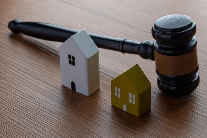 Mazo de juez junto a dos casas en miniatura, simbolizando el reparto de bienes inmuebles en una herencia o divorcio
