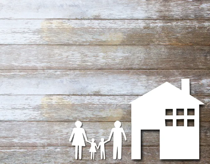Silueta de familia (padre, madre e hijos) y una casa sobre fondo de madera, representando el derecho de familia y la herencia