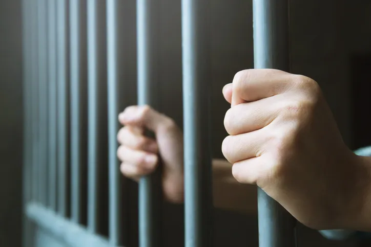 Manos sujetando los barrotes de una celda de prisión, simbolizando la privación de libertad.