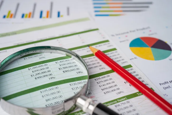 Lupa sobre un informe financiero con cifras y gráficos, representando la revisión o análisis de datos económicos.