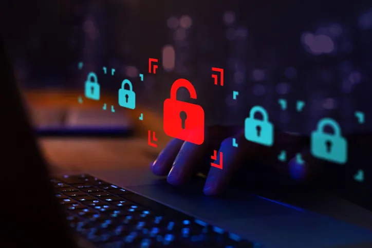 Mano sobre un teclado de portátil junto a iconos de candados, uno abierto en rojo, representando una vulneración de seguridad informática o ciberataque.