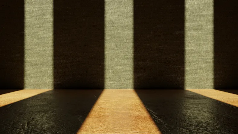 Fondo abstracto con franjas de luz y sombra proyectadas sobre una pared de tela y un suelo de madera oscura.