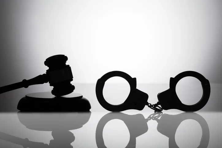Silueta de un mazo de juez y unas esposas sobre una superficie reflectante, simbolizando la justicia penal y sus consecuencias legales.