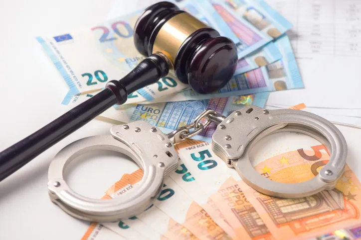 Mazo de juez y esposas sobre billetes de euro, representando un delito patrimonial y su consecuencia penal.