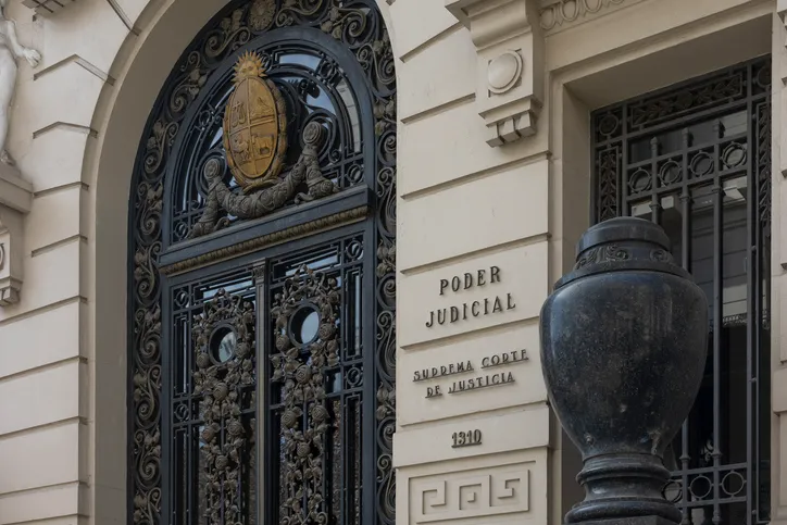 Fachada de un edificio judicial con puerta de hierro ornamentada y el rótulo 'Poder Judicial - Suprema Corte de Justicia'.
