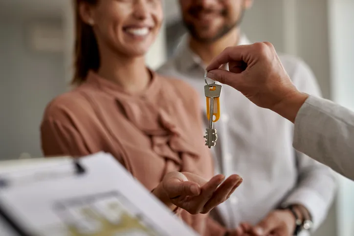 Pareja sonriente recibiendo las llaves de su nueva vivienda de manos de un agente inmobiliario.