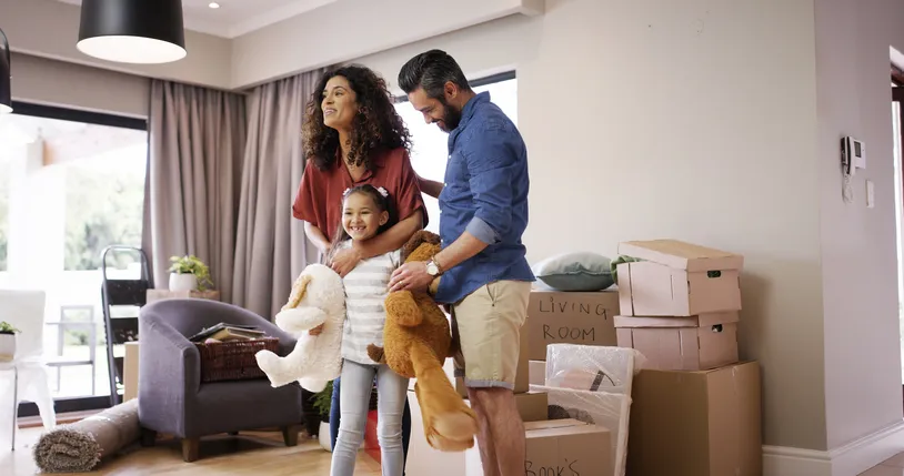 Familia con una niña sonriente en un salón rodeado de cajas de mudanza, disfrutando de su nuevo hogar.