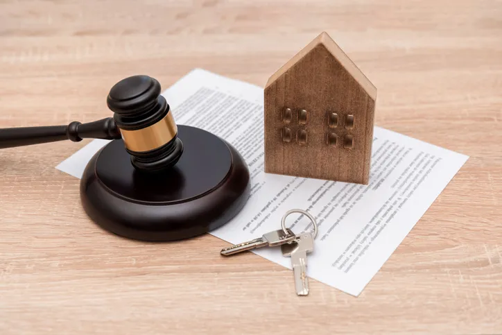 Mazo de juez, una maqueta de casa y unas llaves sobre un documento legal, representando un litigio o proceso judicial relacionado con la vivienda.