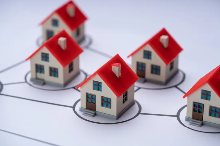 Miniaturas de casas idénticas conectadas entre sí por líneas, representando una comunidad de propietarios o un conjunto residencial.